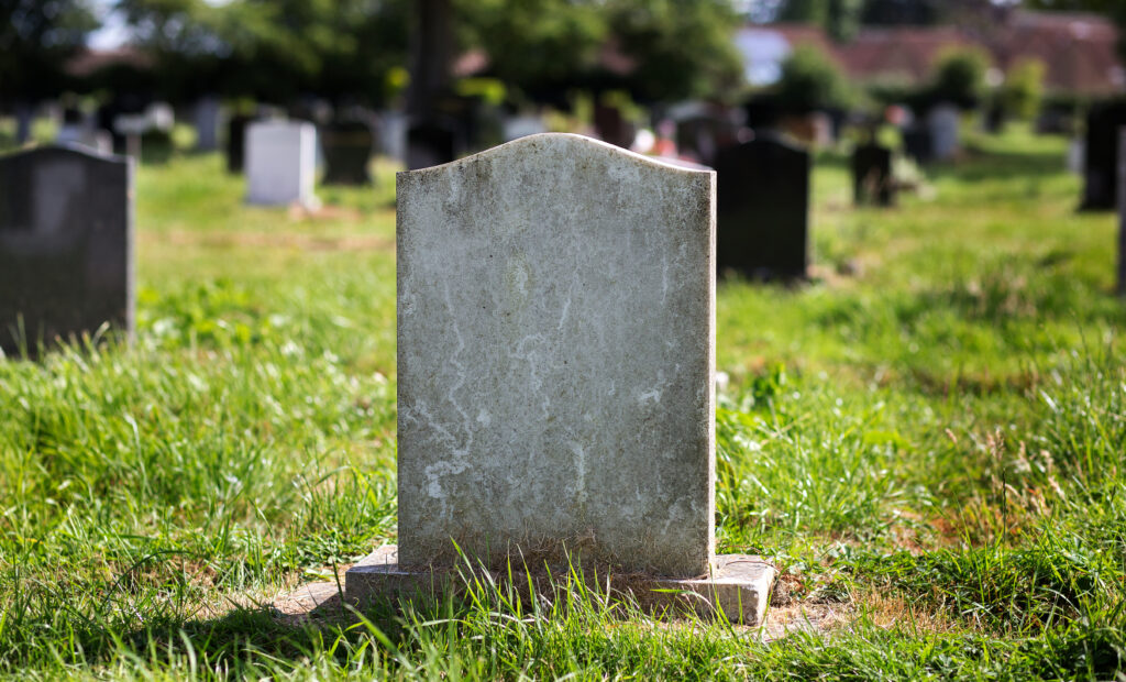 A grey tombstone in a grassy graveyard with other tombstones in the background.